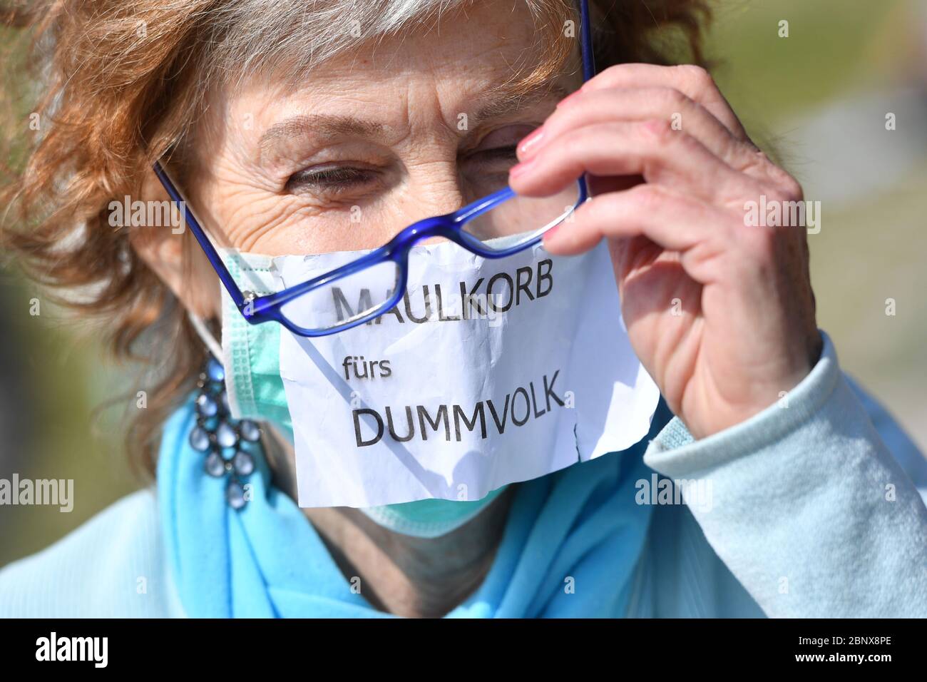 Dimostrazione contro corona restrizioni su Theresienwiese a Monaco il 16 maggio 2020. Dimostranti, dimostrazione sul Bavariaring- una donna con una maschera facciale, maschera sulla quale è allegata una nota: MAULKORB FUERS DUMMVOLK. | utilizzo in tutto il mondo Foto Stock