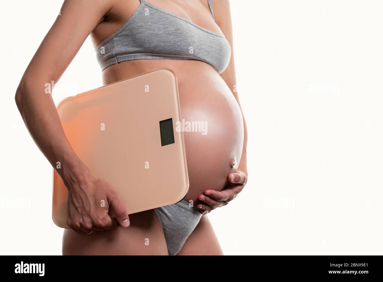 donna incinta che tiene la bilancia su uno sfondo bianco Foto Stock