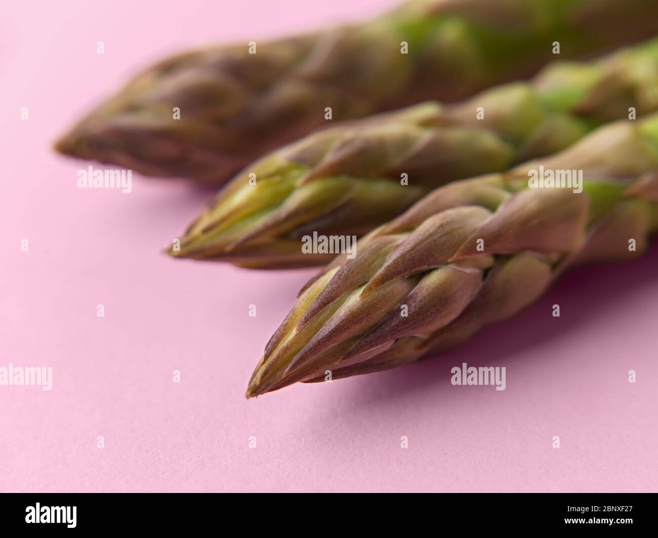 Macrofotografia della parte superiore di stocchi di asparagi verdi freschi su sfondo rosa pastello. Ingrediente per mangiare l'healhy, vegetariano e cibo crudo Foto Stock