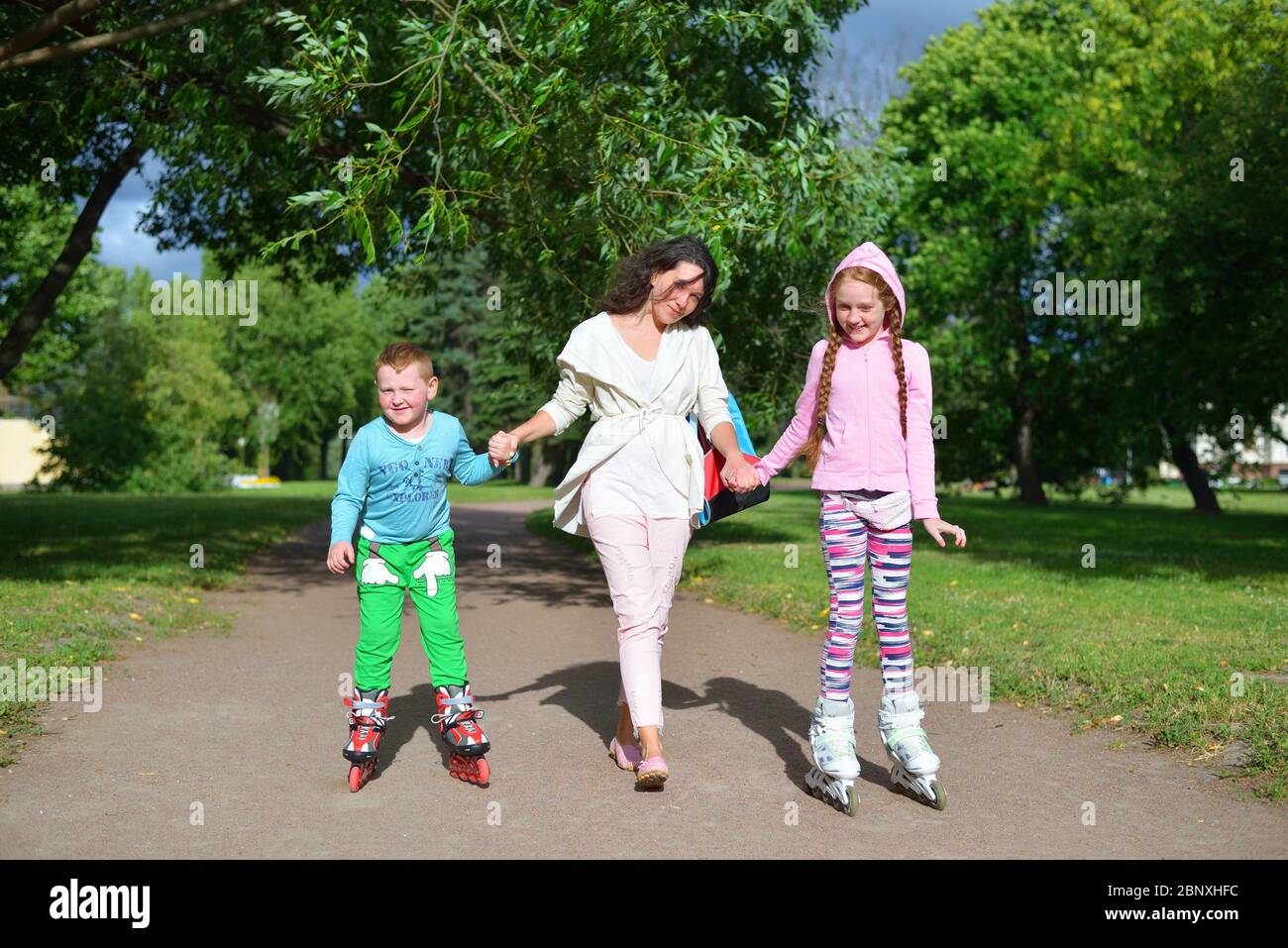 Donna guida la mano dei bambini sorridenti sui pattini a rotelle nel parco a San Pietroburgo Foto Stock