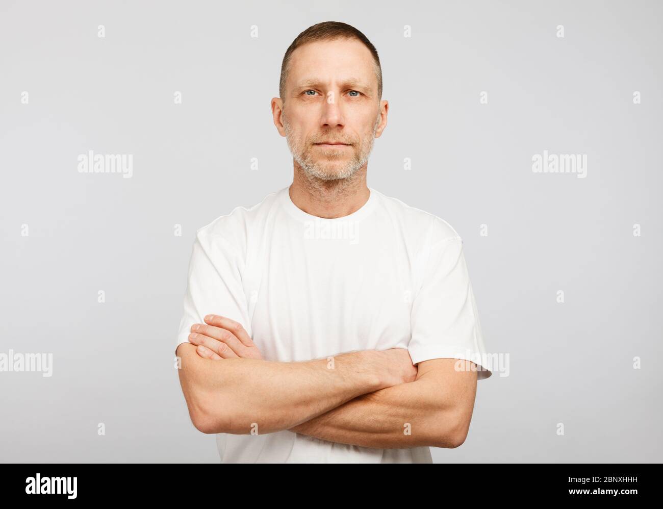 Uomo in T-shirt bianca con braccia incrociate su sfondo bianco. Foto Stock