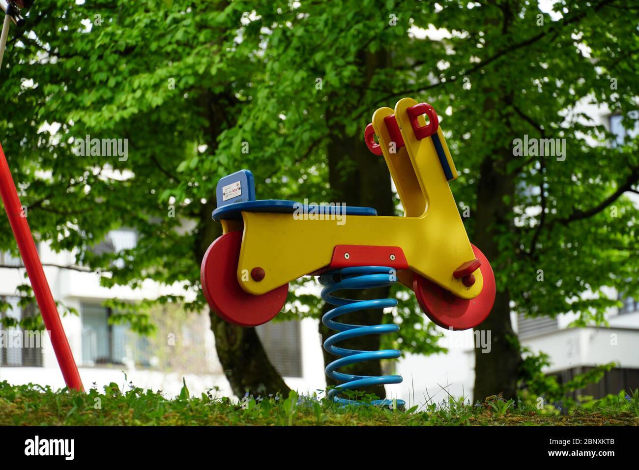 una moto dondolante in primavera, un giocattolo in legno stilizzato in rosso e giallo per i bambini piccoli su una spessa molla di metallo, è calato a terra su un cortile Foto Stock