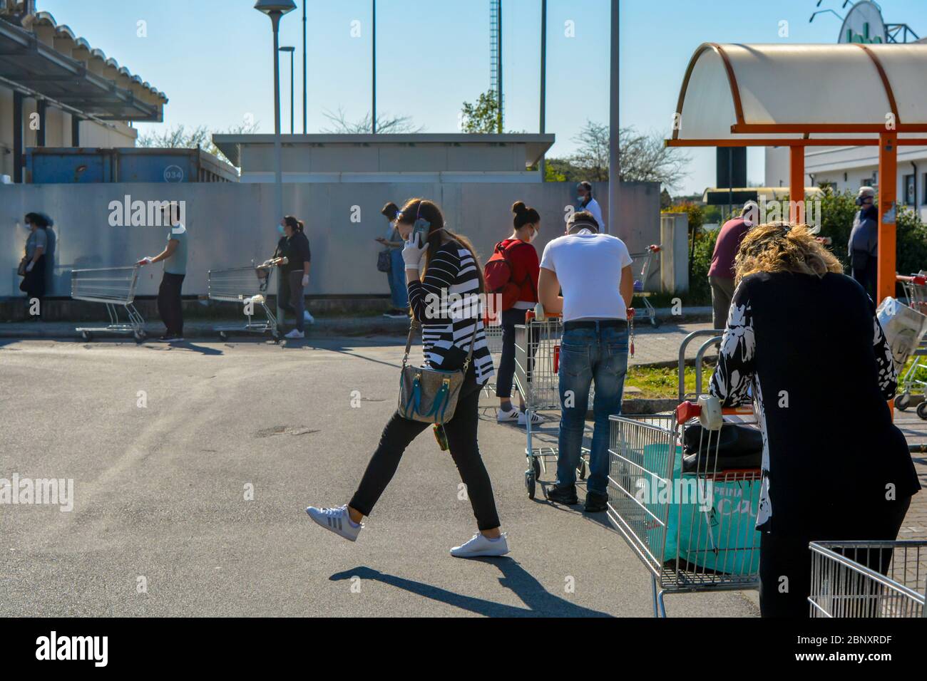 Toscana, Italia, 04/08/20: Una ragazza italiana con guanti protettivi coronavirus impegnata a chiamare il suo smartphone vicino a una linea di persone in linea per le grocerie Foto Stock