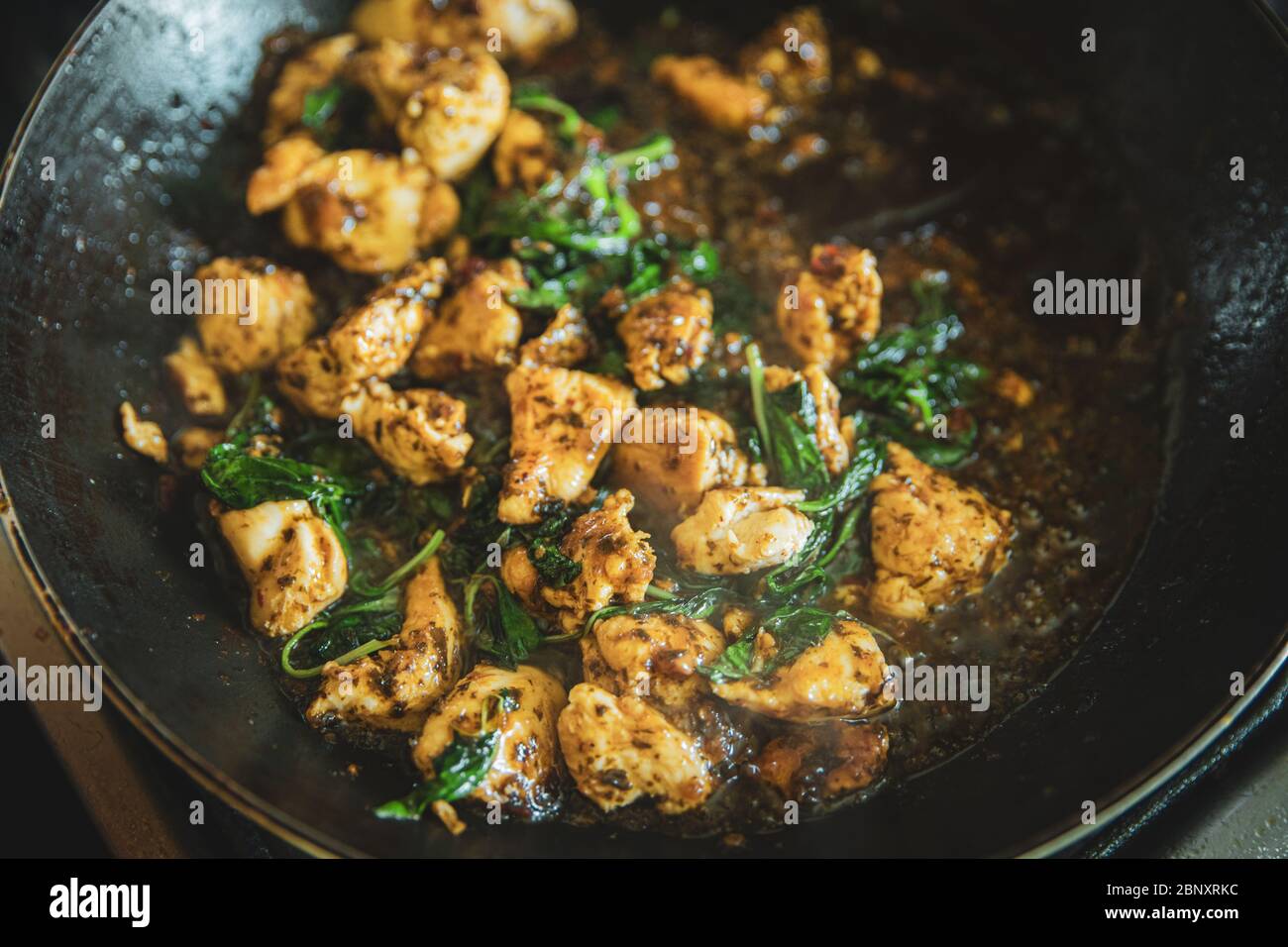 Scacchi di basilico tailandese in padella, tradizionale pasto fritto in padella, costolette di carne di pollo con frittura di foglie di basilico verde da vicino Foto Stock