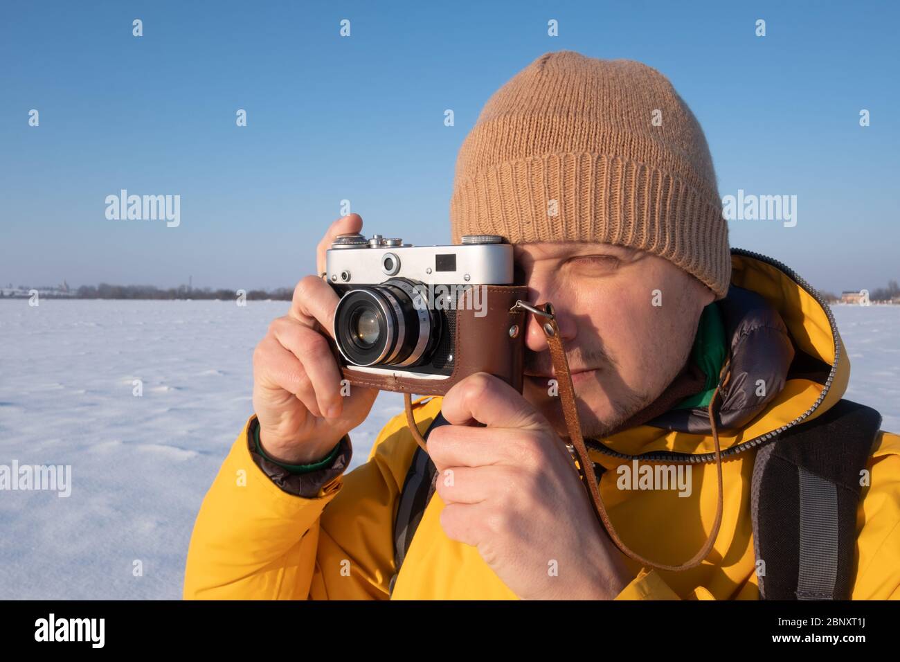 Fotografo in giacca gialla prendendo foto sulla neve campo invernale Foto Stock