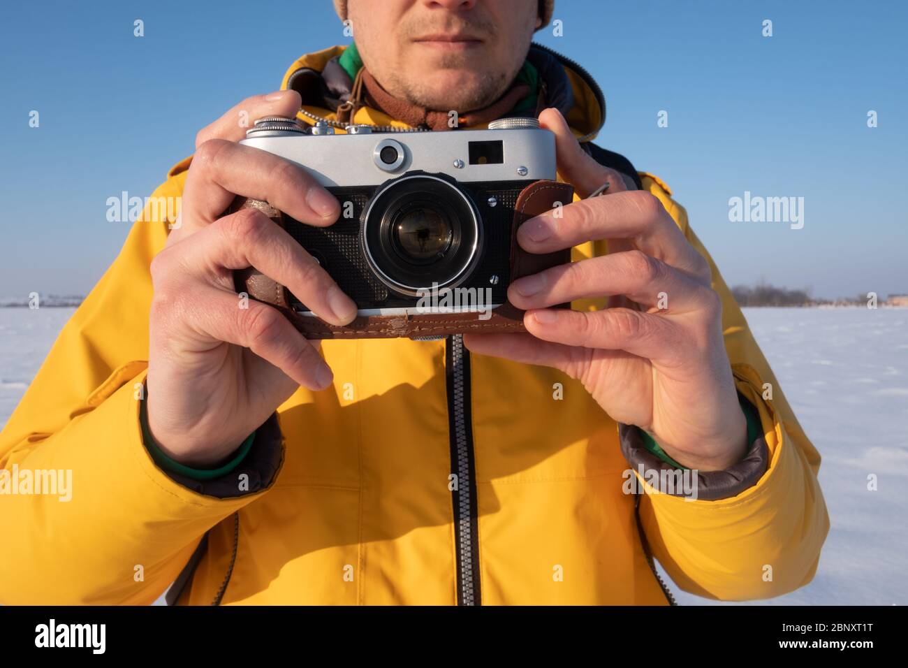 Fotografo in giacca gialla prendendo foto sulla neve campo invernale Foto Stock