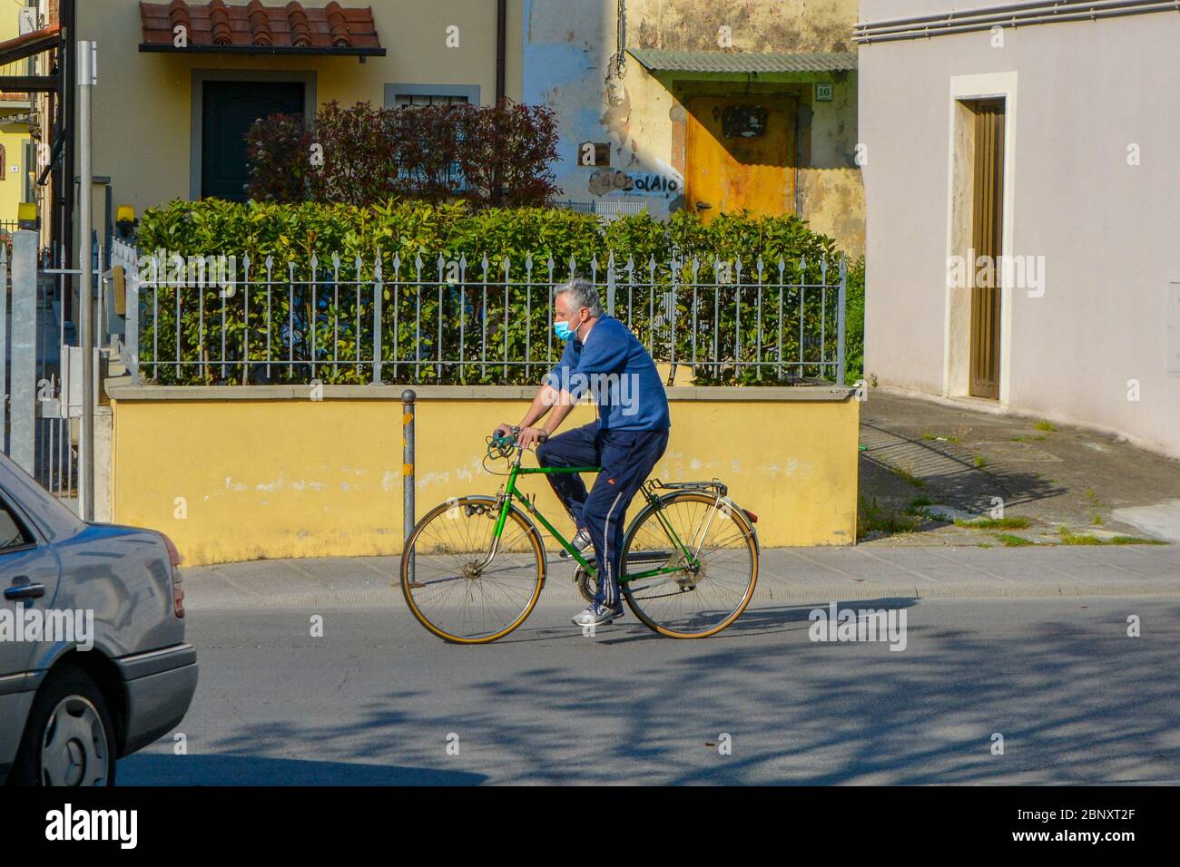 Un uomo bianco italiano che indossa una maschera protettiva COVID-19 che cavalca la sua bicicletta nel centro della città. Scene quotidiane di sport e fitness urbano durante il coronavirus Foto Stock