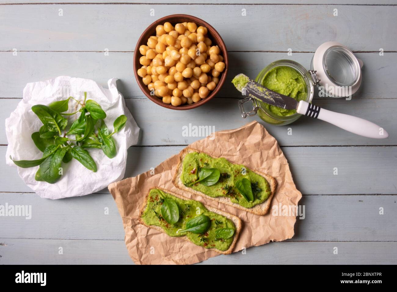 Due cracker con humus di spinaci verdi su tavola di legno. Disposizione piatta. Concetto di hummus. Fotografia di cibo Foto Stock