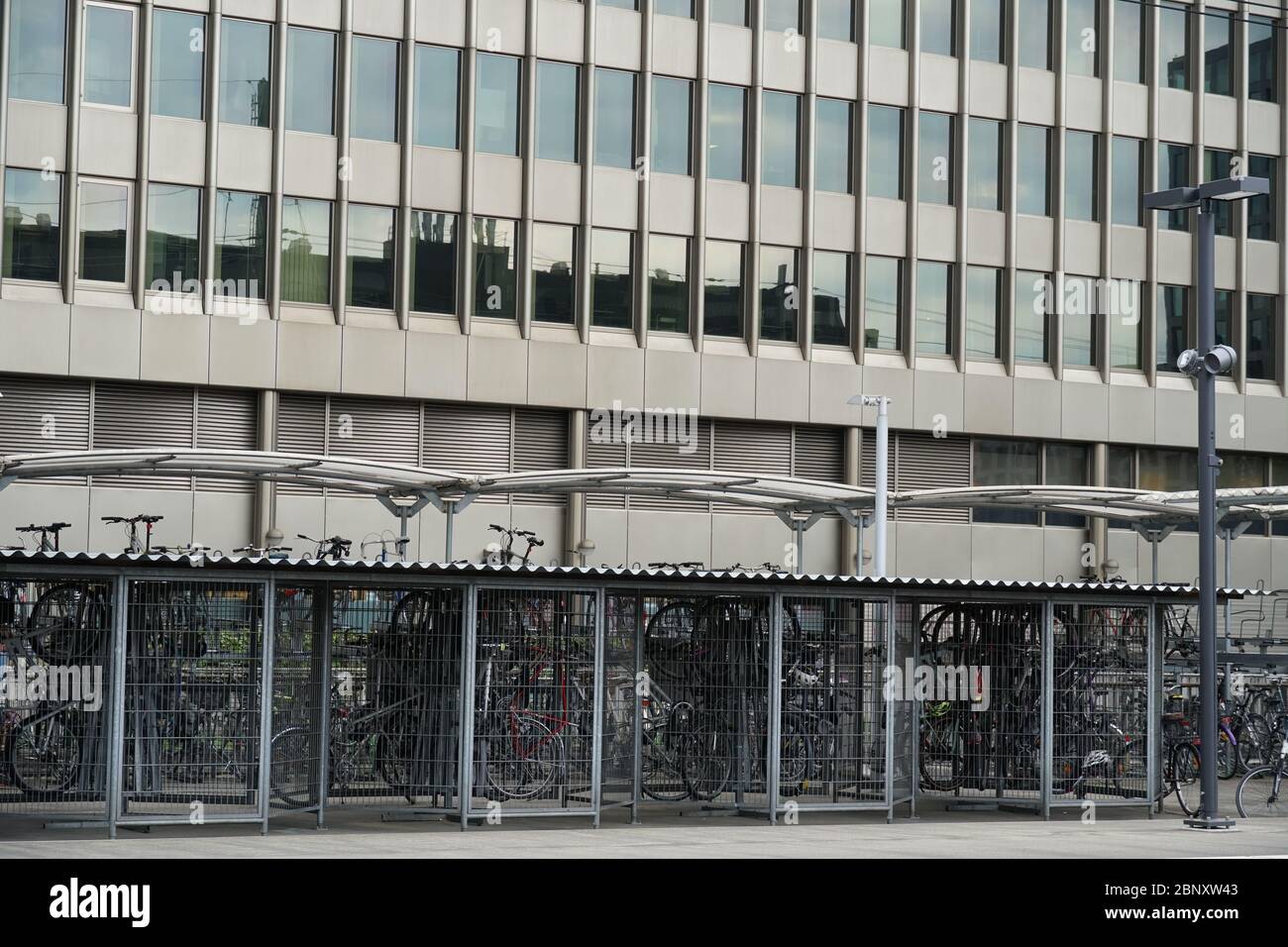 Soluzioni di parcheggio per biciclette vicino alla stazione ferroviaria con un edificio aziendale sullo sfondo. Questo sistema incoraggia gli spostamenti ecologici Foto Stock