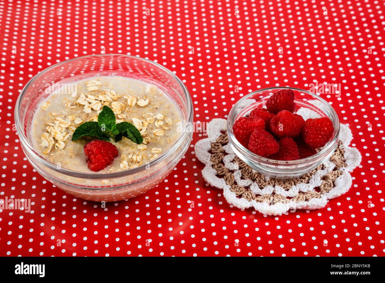 Porridge di farinata d'avena con lamponi e foglie di menta. Sfondo rosso con punti bianchi. Foto Stock