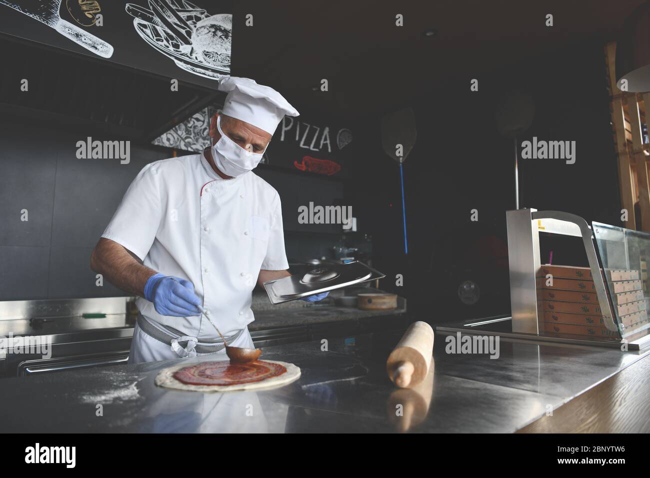 Chef esperto che prepara la tradizionale pizza italiana all'interno della moderna cucina del ristorante con speciale forno a legna. Indossare medico protettivo fa Foto Stock