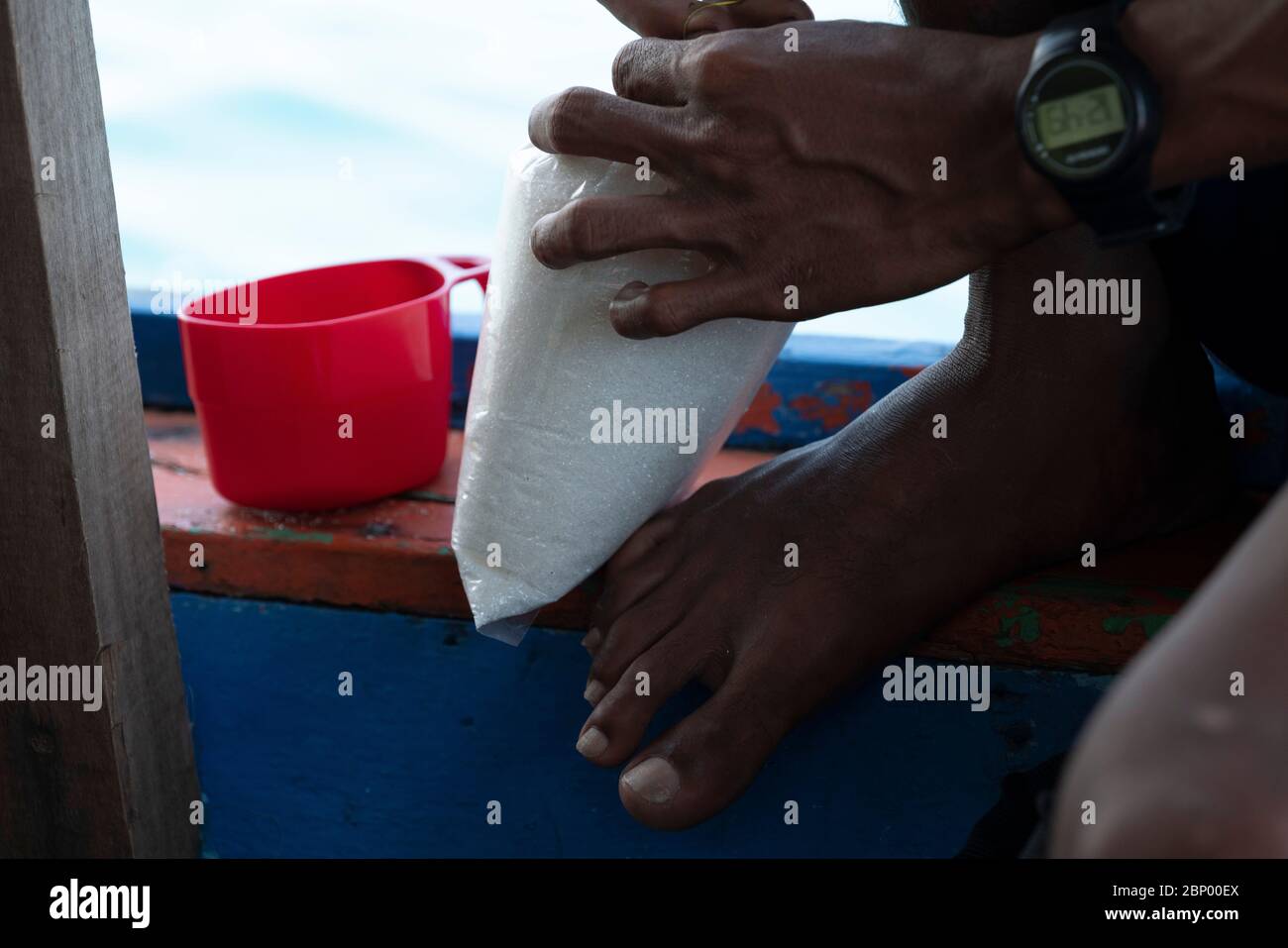 Un barman che apre la borsa dello zucchero per aggiungere un po' di tazzina di plastica rossa per la sua preparazione del caffè Foto Stock