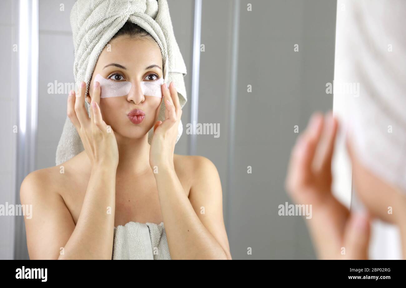 Bella donna che applica la maschera sotto gli occhi anti-affaticamento baciandosi nello specchio nel bagno. Cura della pelle ragazza toccare le macchie di tessuto maschera sotto Foto Stock