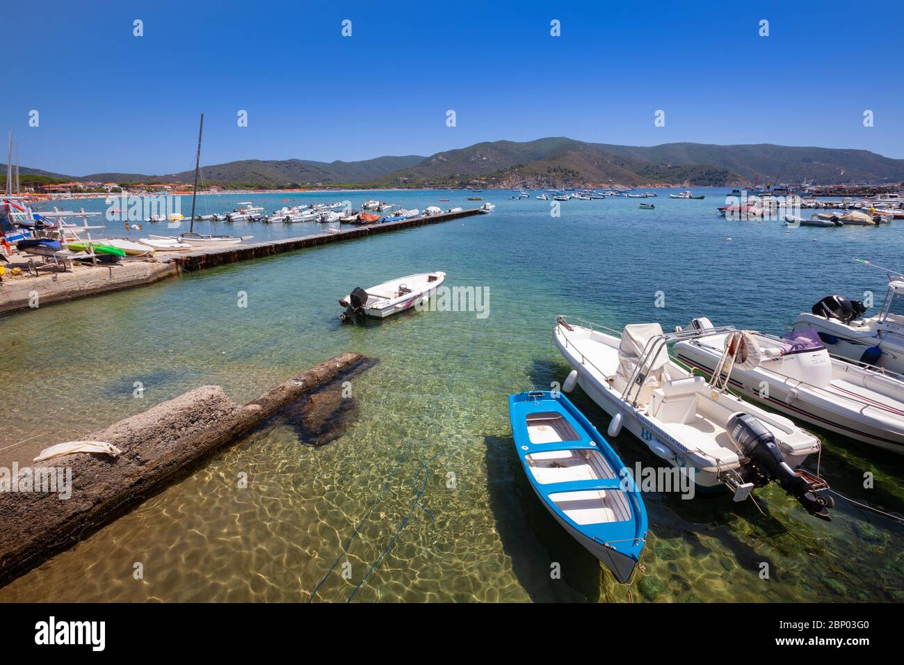 Marina di campo, Italia. 25 giugno 2016: Piccolo porto con barche ancorate al molo nel mare dell'Isola d'Elba. Lunga banchina. Case, montagne e. Foto Stock
