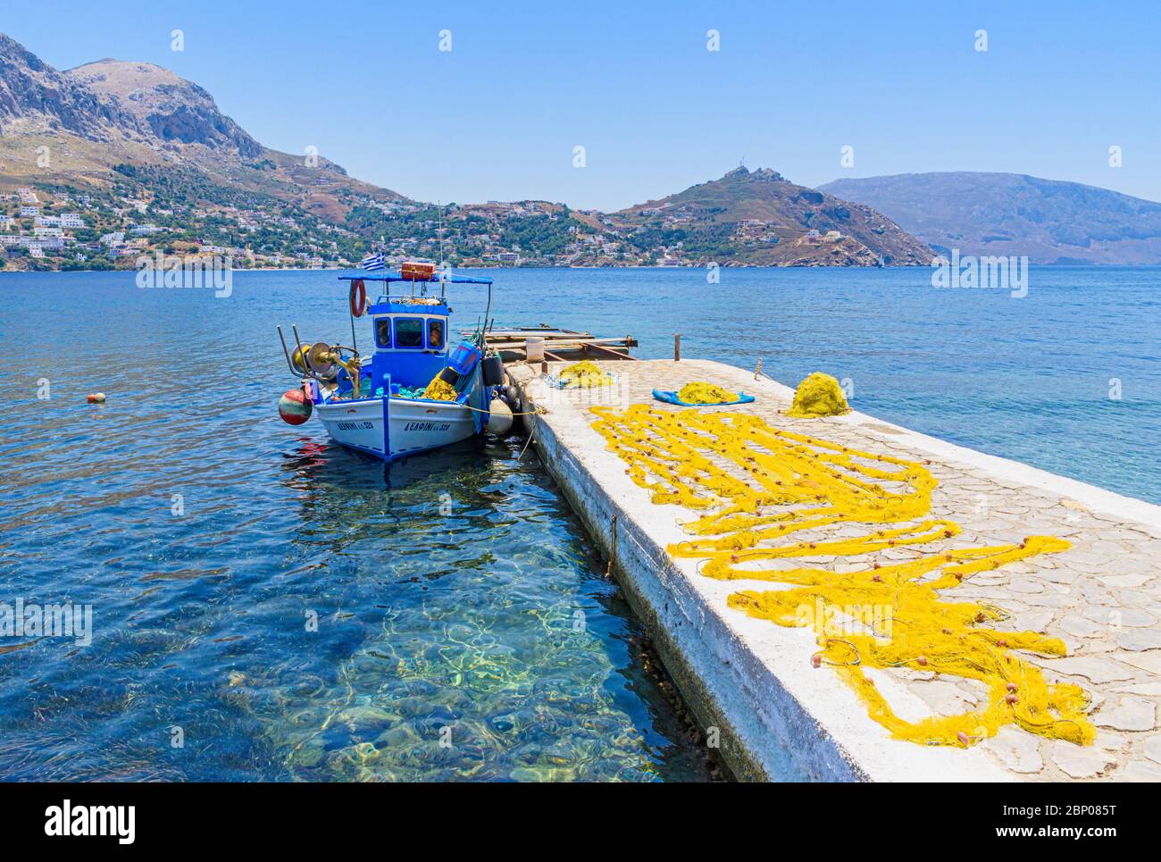 Barche da pesca e reti gialle che asciugano sul molo della piccola città portuale di Telendos Island, Kalymnos, Dodecanese, Grecia Foto Stock