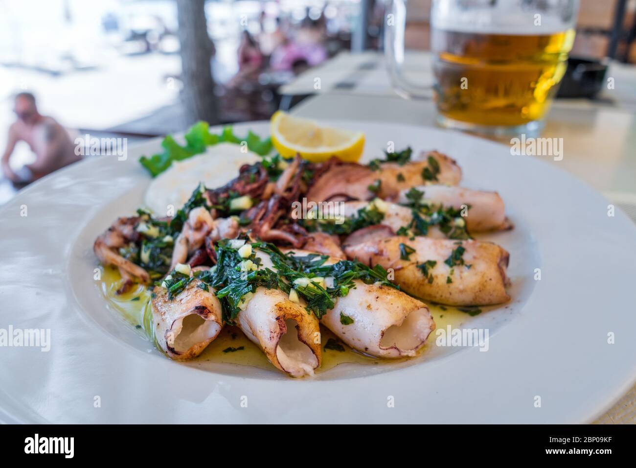 Calamari grigliati con erbe, aglio e limone su piatto bianco da vicino. Popolare e delizioso pasto mediterraneo. Foto Stock