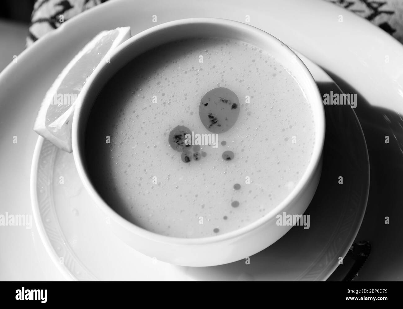 Zuppa tradizionale turca con purè di lenticchie (Turk Mercimek Çorbasi) su recipiente in ceramica bianca e fetta di limone sul piatto. Immagine con toni in bianco e nero. Co. Alta Foto Stock