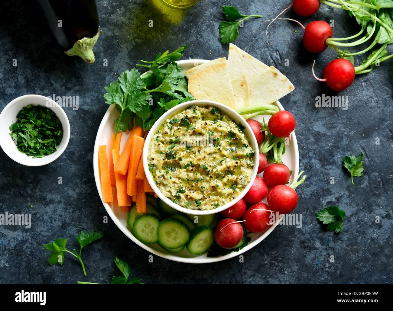 Baba ganoush (salsa di melanzane arrostite) in ciotola e verdure biologiche fresche su sfondo di pietra blu. Mangiare sano. Cucina vegetariana vegana. A Foto Stock