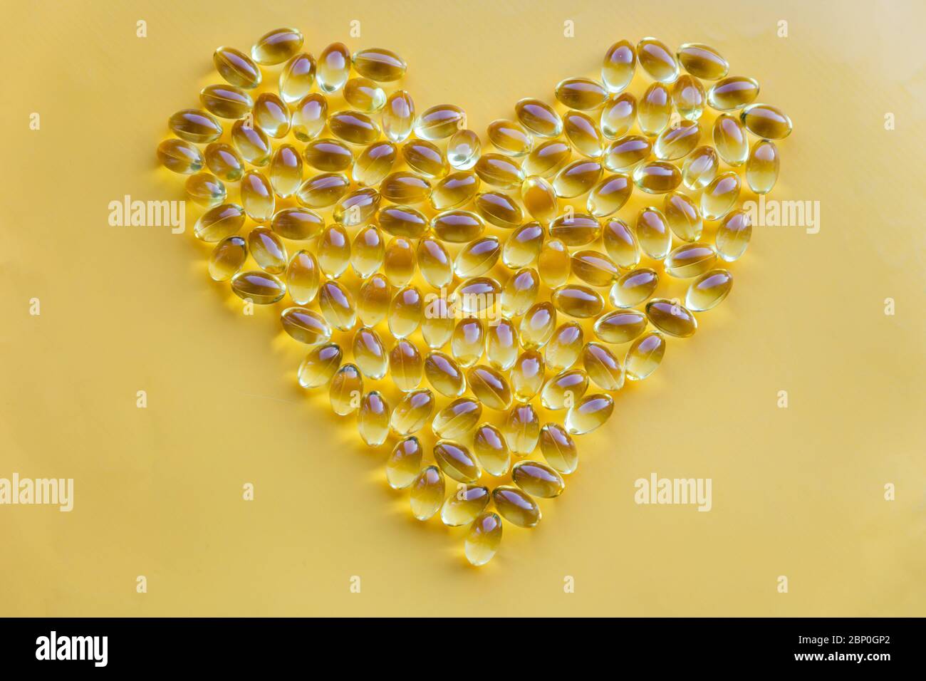 Forma cardiaca di integratori vitaminici gialli, omega 3 capsule, affettuosa salute dietetica su sfondo luminoso con spazio di copia Foto Stock