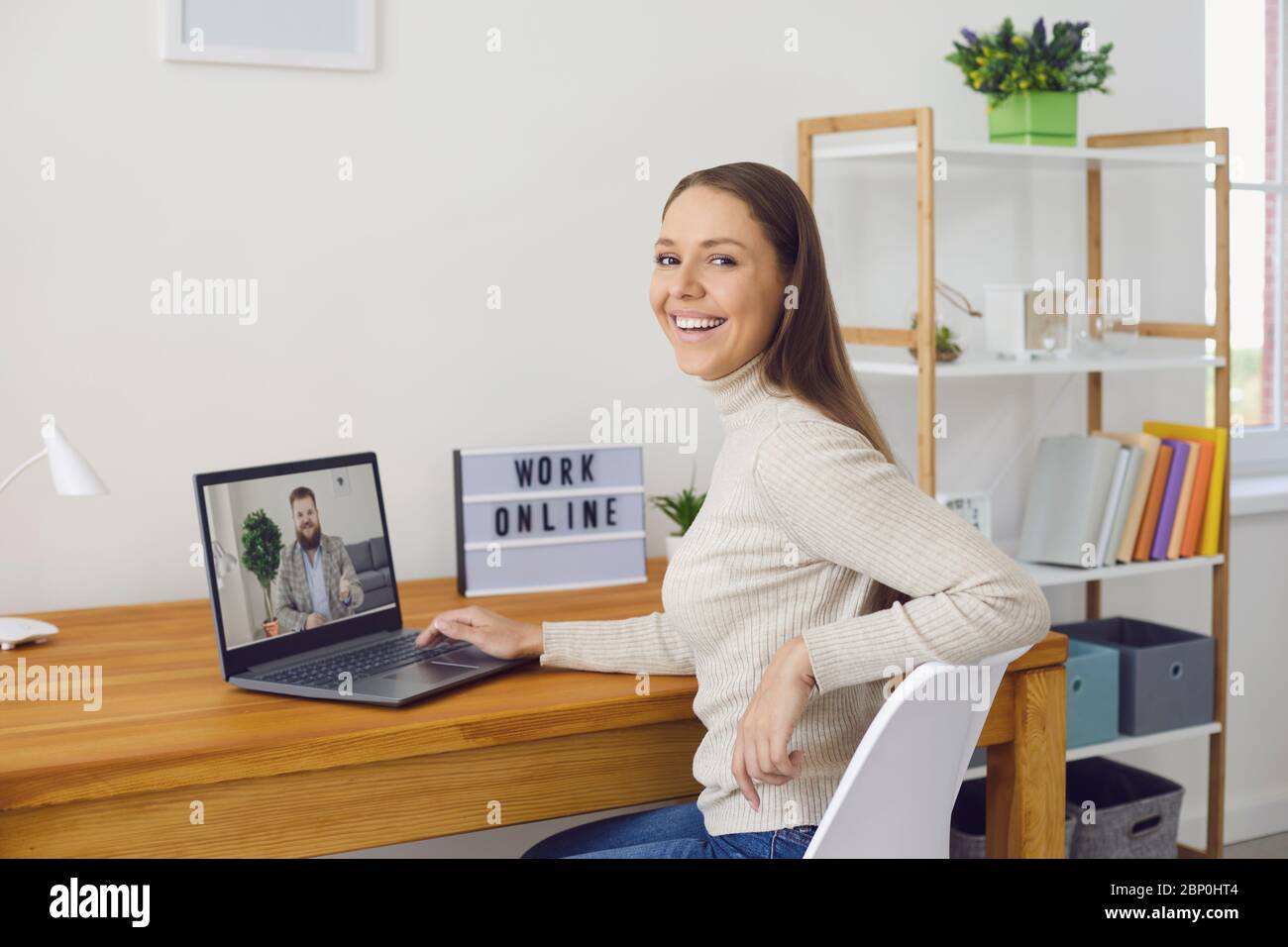 Lavoro online a casa. Una donna lavora a un tavolo utilizzando un computer portatile e parla con un partner tramite l'applicazione di chat per videochiamata a casa. Foto Stock