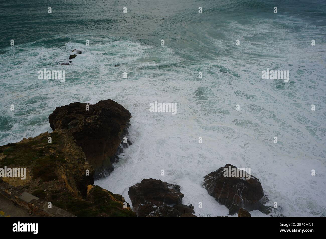 Le onde si stanno rompendo nella roccia a Nazare Foto Stock