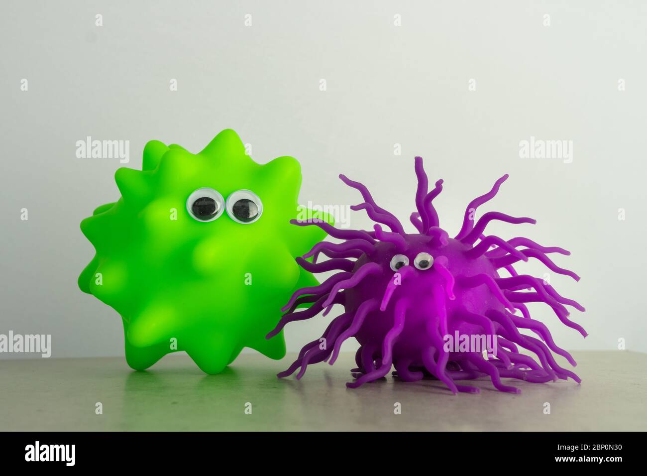 Un giocattolo verde per il cane e una palla gummia viola con gli occhi come una rappresentazione di virus o batteri Foto Stock