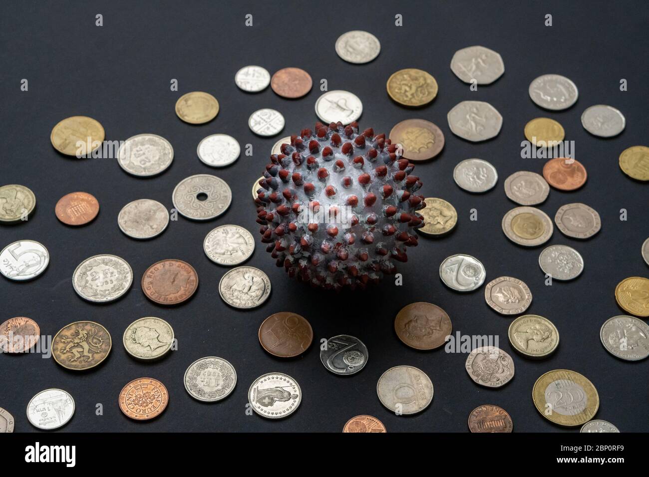 Una palla dipinta come un virione SARS-COV-2 al centro di molte monete provenienti da diversi paesi Foto Stock