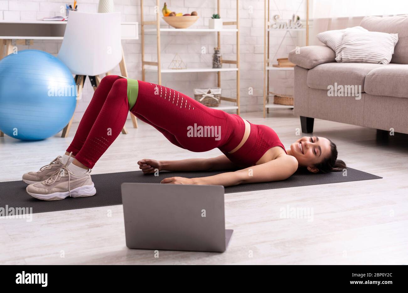 Allenamento domestico interattivo. Ragazza latina che guarda in diretta streaming allenamento e facendo esercizio abs con elastico, in interni Foto Stock