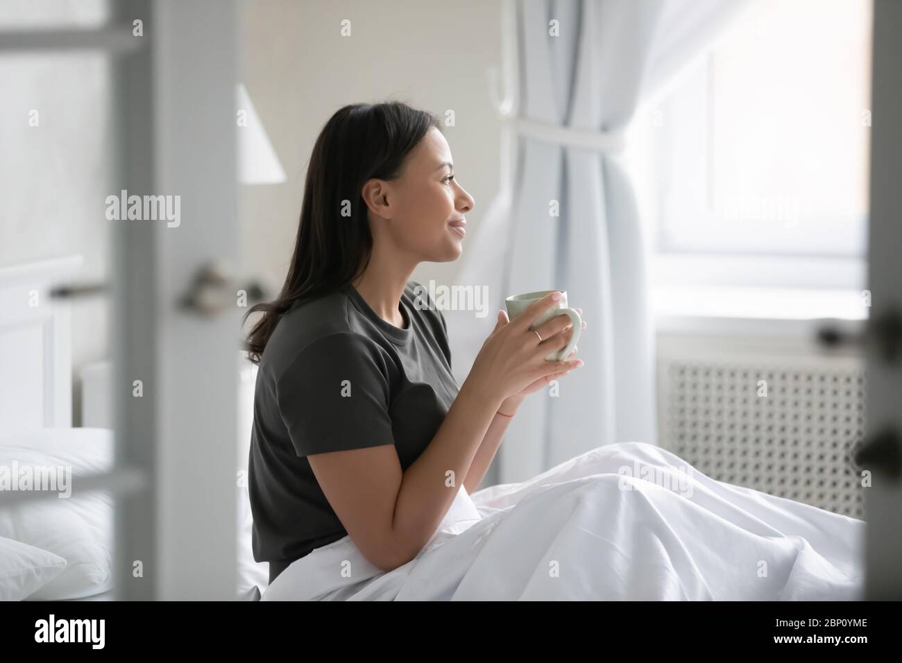 Donna africana sveglia seduta a letto bevendo caffè del mattino Foto Stock