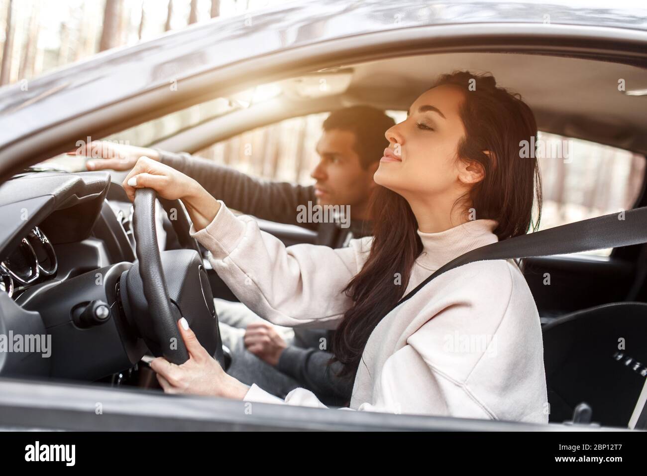 Istruzioni di guida. Una giovane donna impara a guidare una macchina per la prima volta. Il suo istruttore o ragazzo la aiuta e le insegna. Foto Stock