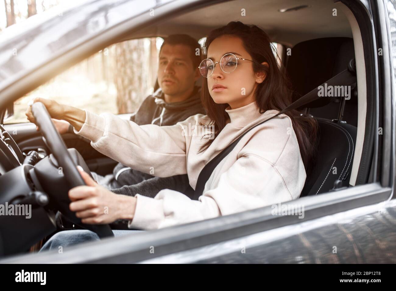 Istruzioni di guida. Una giovane donna impara a guidare una macchina per la prima volta. Il suo istruttore o ragazzo la aiuta e le insegna. Foto Stock