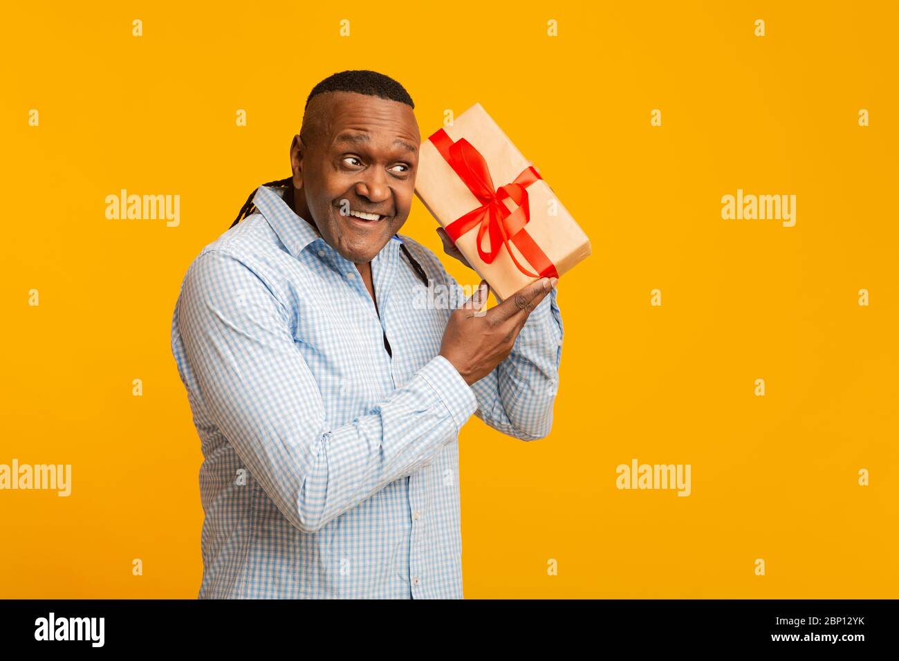 Curioso uomo afroamericano maturo scuotere presente scatola Foto Stock