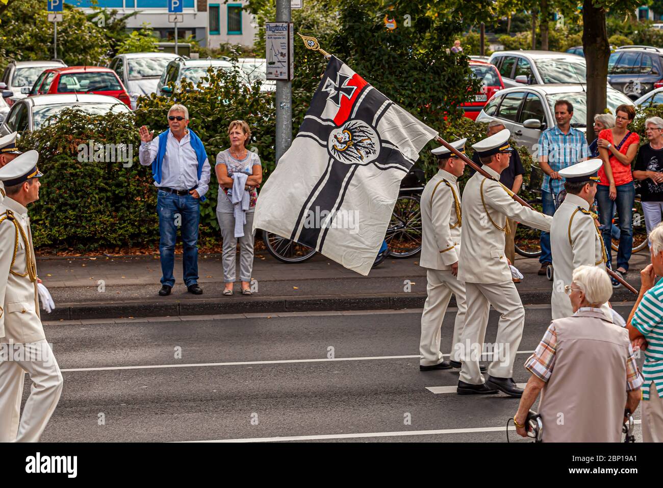 I membri di un'associazione di veterani della marina portano l'alfiere storico della Marina imperiale tedesca durante una parata del festival dei tiratori a Grevenbroich, in Germania – una tradizionale festa tedesca dei tiratori. Il disegno, una croce di ferro e un aquila su campo bianco, è stato utilizzato dal 1903 al 1921. Due passanti salutano i marciatori Foto Stock