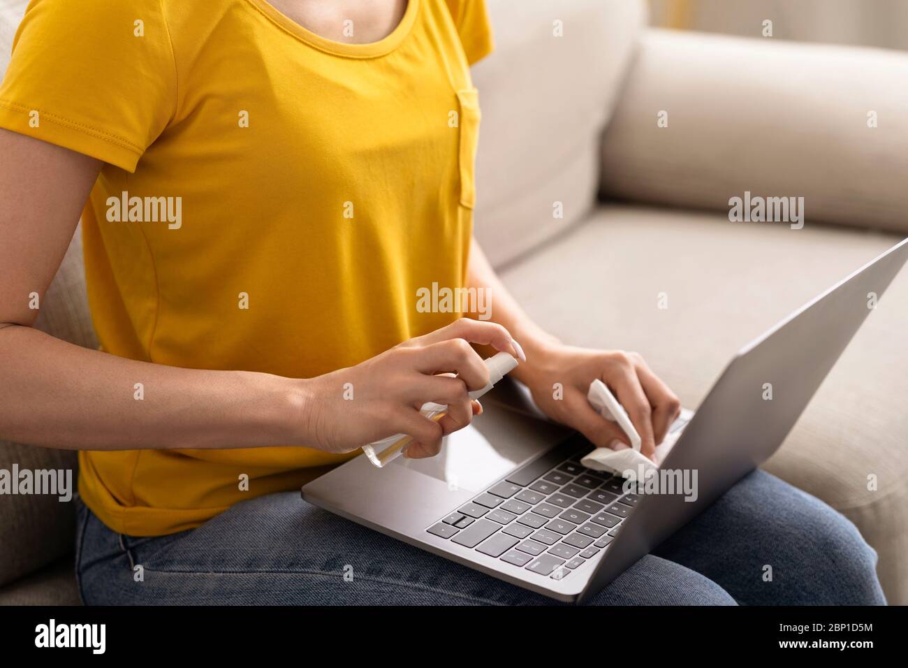 Igiene contro le infezioni. Ragazza irriconoscibile che usa l'igienizzatore per pulire il laptop a casa, primo piano Foto Stock