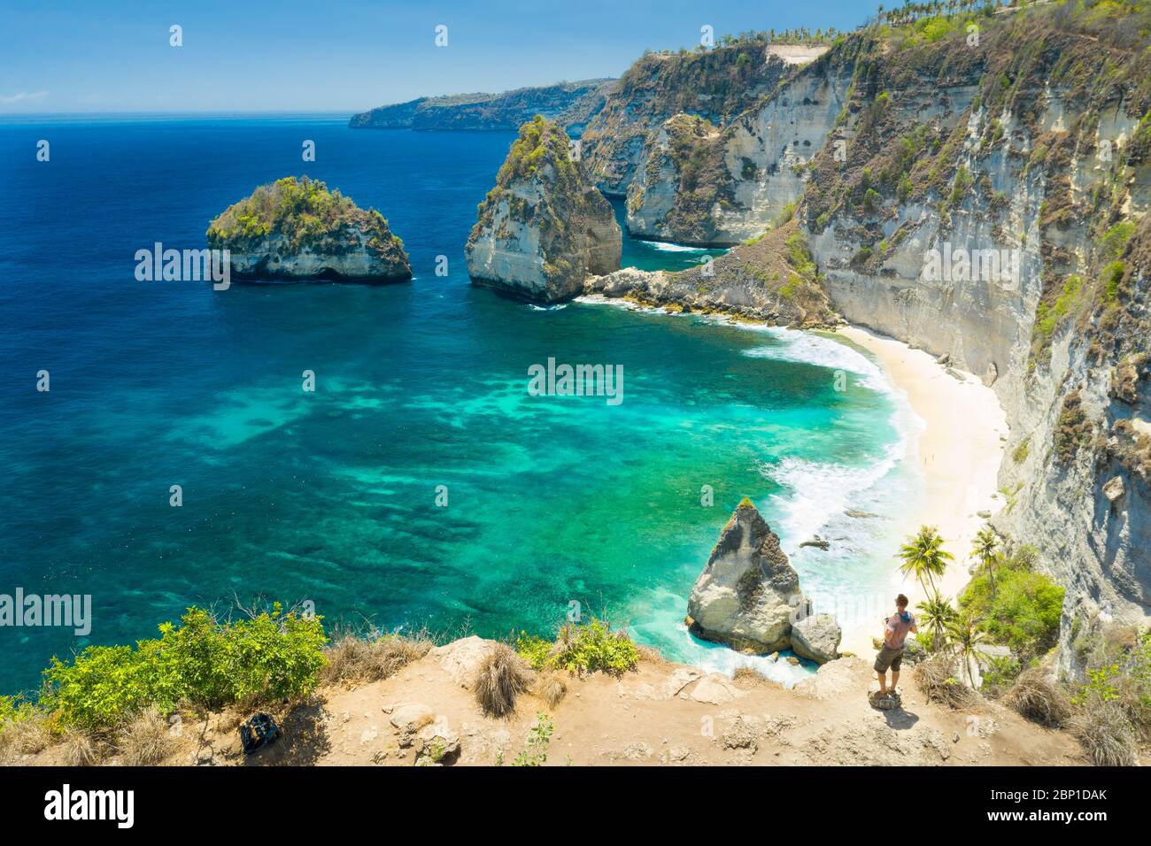 Uomo viaggiatore in piedi sulla cima della montagna guardare l'oceano e le rocce. Concetto di viaggio e stile di vita attivo. Avventura e viaggio a Bali, Indonesia. Foto Stock