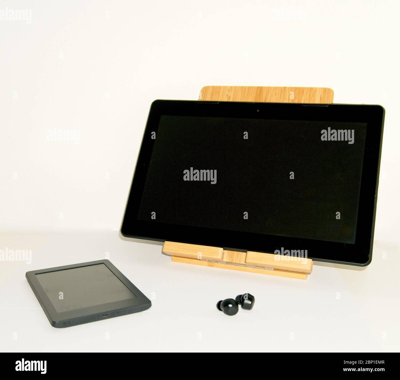 Ancora più vita con un e-book e un tablet su un supporto di sollevamento in legno insieme ad alcune cuffie wireless su sfondo bianco Foto Stock