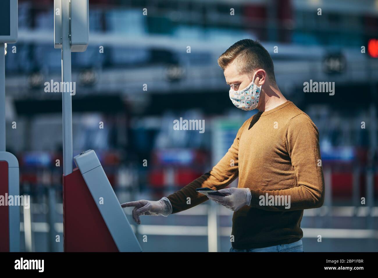 Uomo che indossa la maschera e usa il dispositivo di check-in all'aeroporto. Temi che viaggiano durante la pandemia e la protezione personale. Foto Stock