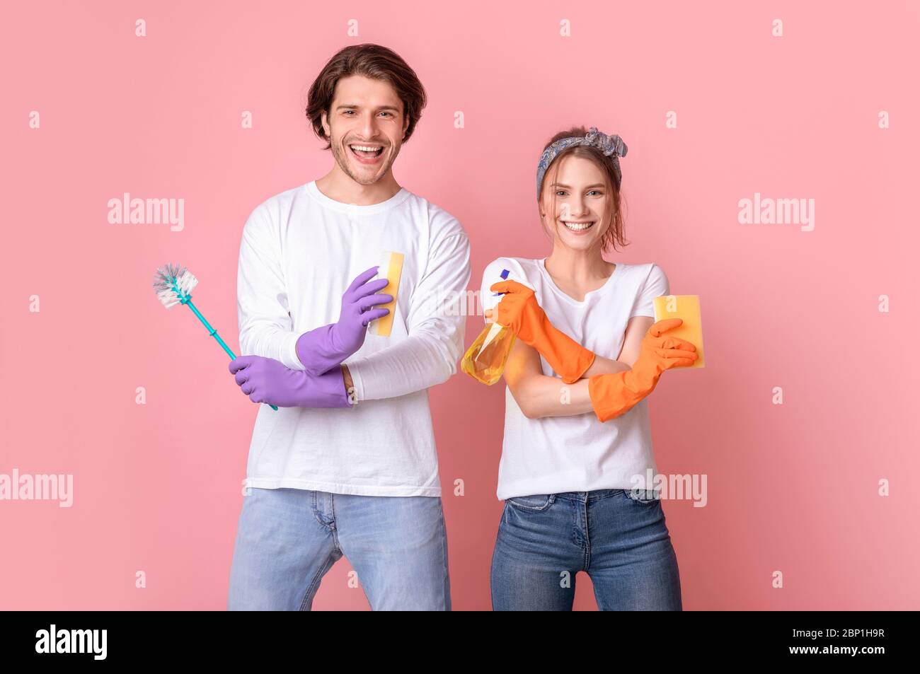 Positivo giovane coniuge che posa con gli attrezzi di pulizia nelle mani sopra sfondo rosa Foto Stock