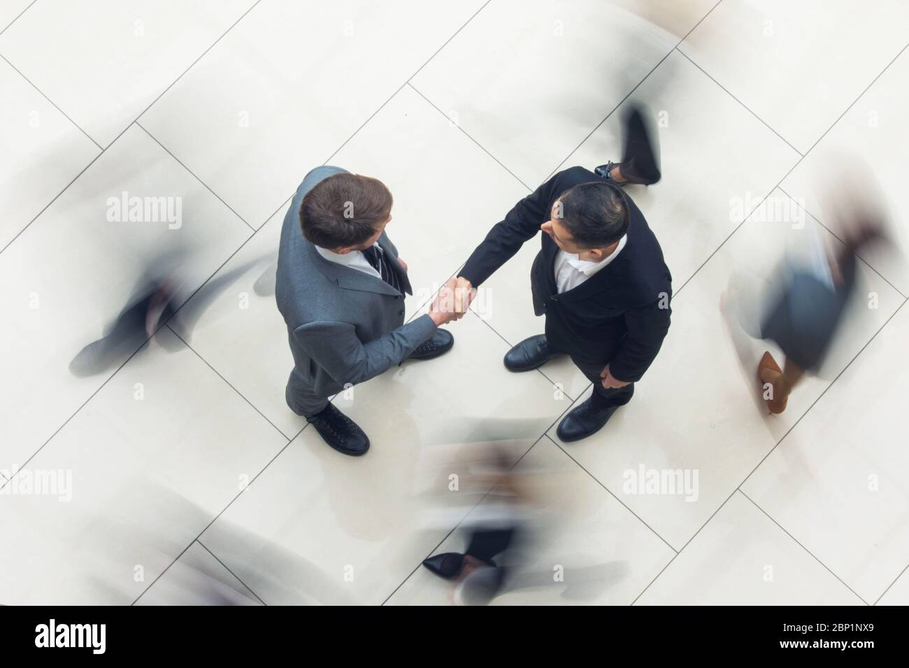 Uomini d'affari che scuotono le mani in piedi in una folla di persone che camminano, vista dall'alto Foto Stock