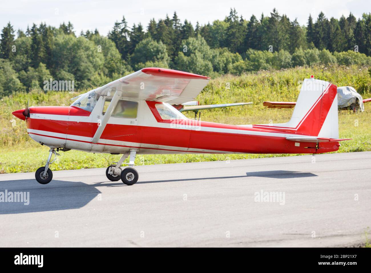 Aereo a due posti con strisce rosse sulla pista sullo sfondo di alberi in una giornata estiva soleggiata Foto Stock