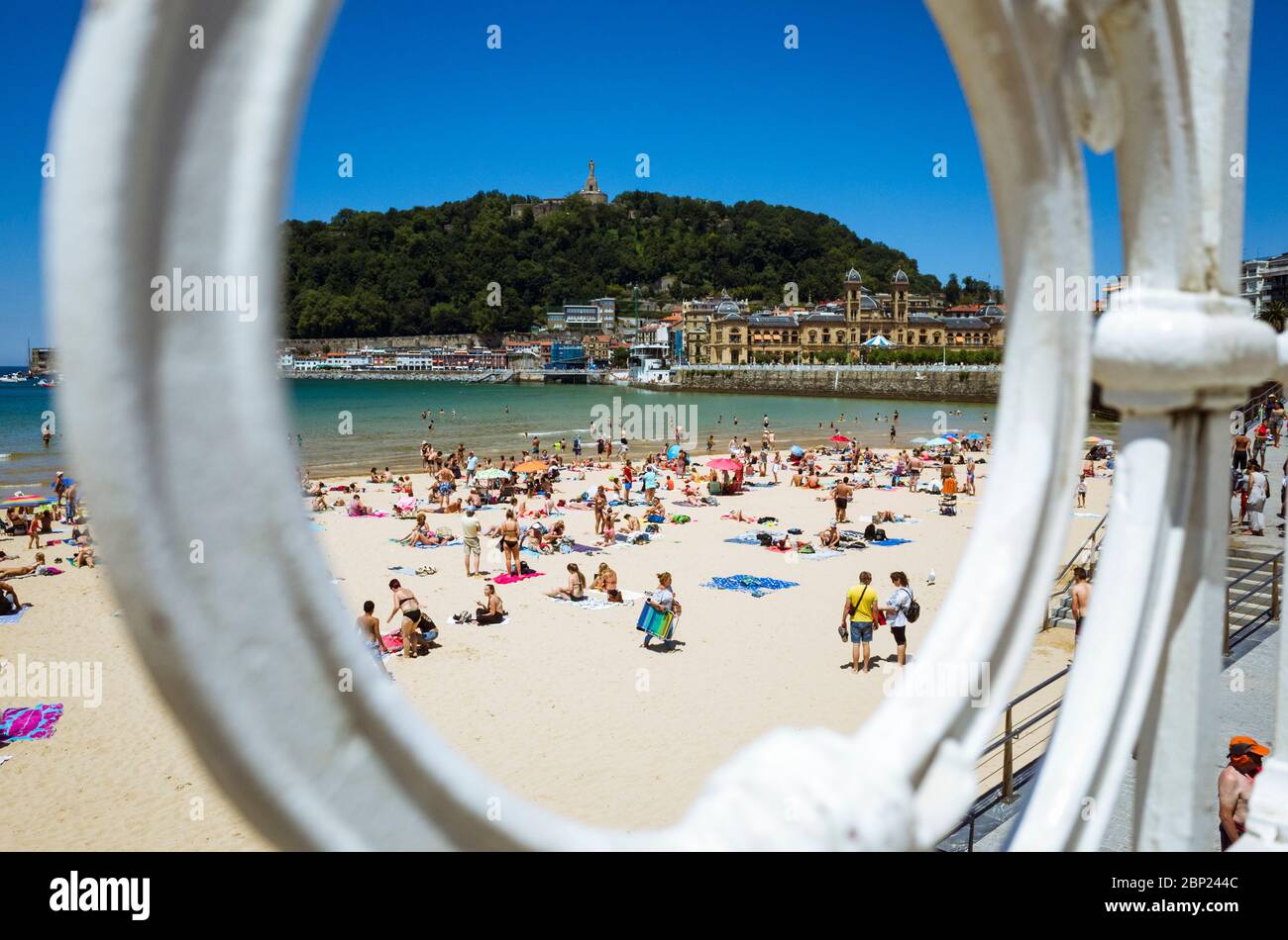 Donostia, Gipuzkoa, Paesi Baschi, Spagna - 12 Luglio 2019 : Vista attraverso il balister iconico della spiaggia di la Concha. Bagnanti e Urgull collina in backg Foto Stock