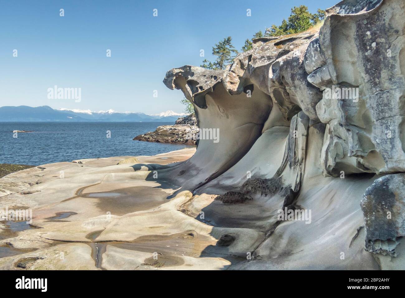 A bassa marea nelle isole Flat Top della British Columbia, archi erosi si stendono su una costa di arenaria liscia, con una vista dello stretto della Georgia e delle Montagne costiere. Foto Stock