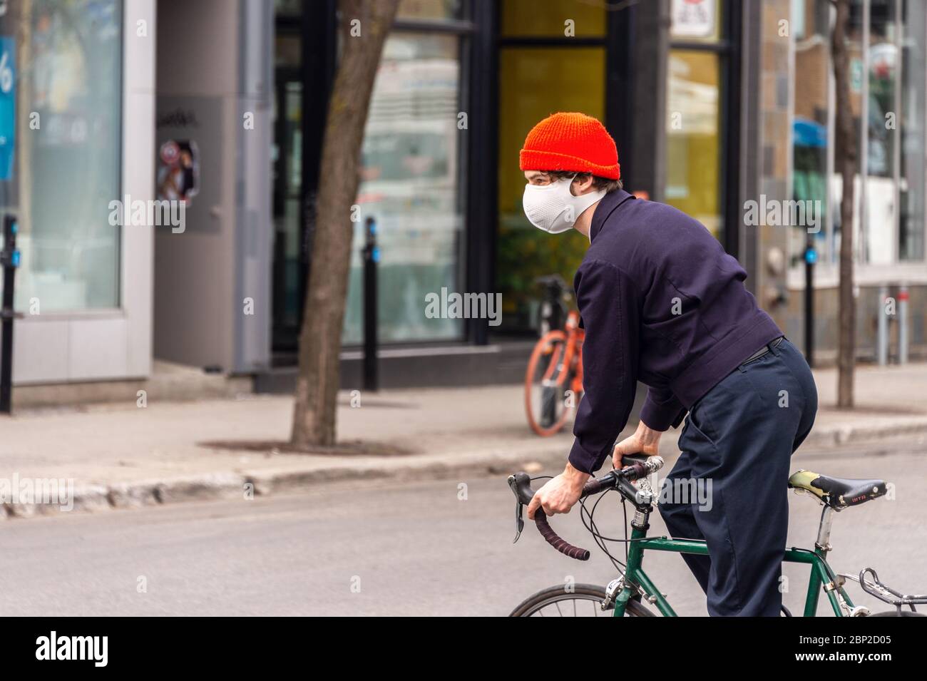 Montreal, CA - 16 maggio 2020: Un giovane con una maschera a cavallo di una bicicletta durante la pandemia del coronavirus COVID-19 su Mont-Royal Avenue. Foto Stock