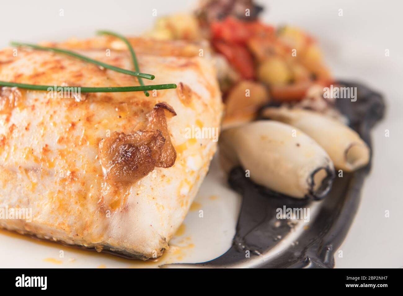 Piatto di nasello cotto con calamari nel suo inchiostro e erba cipollina. Foto Stock