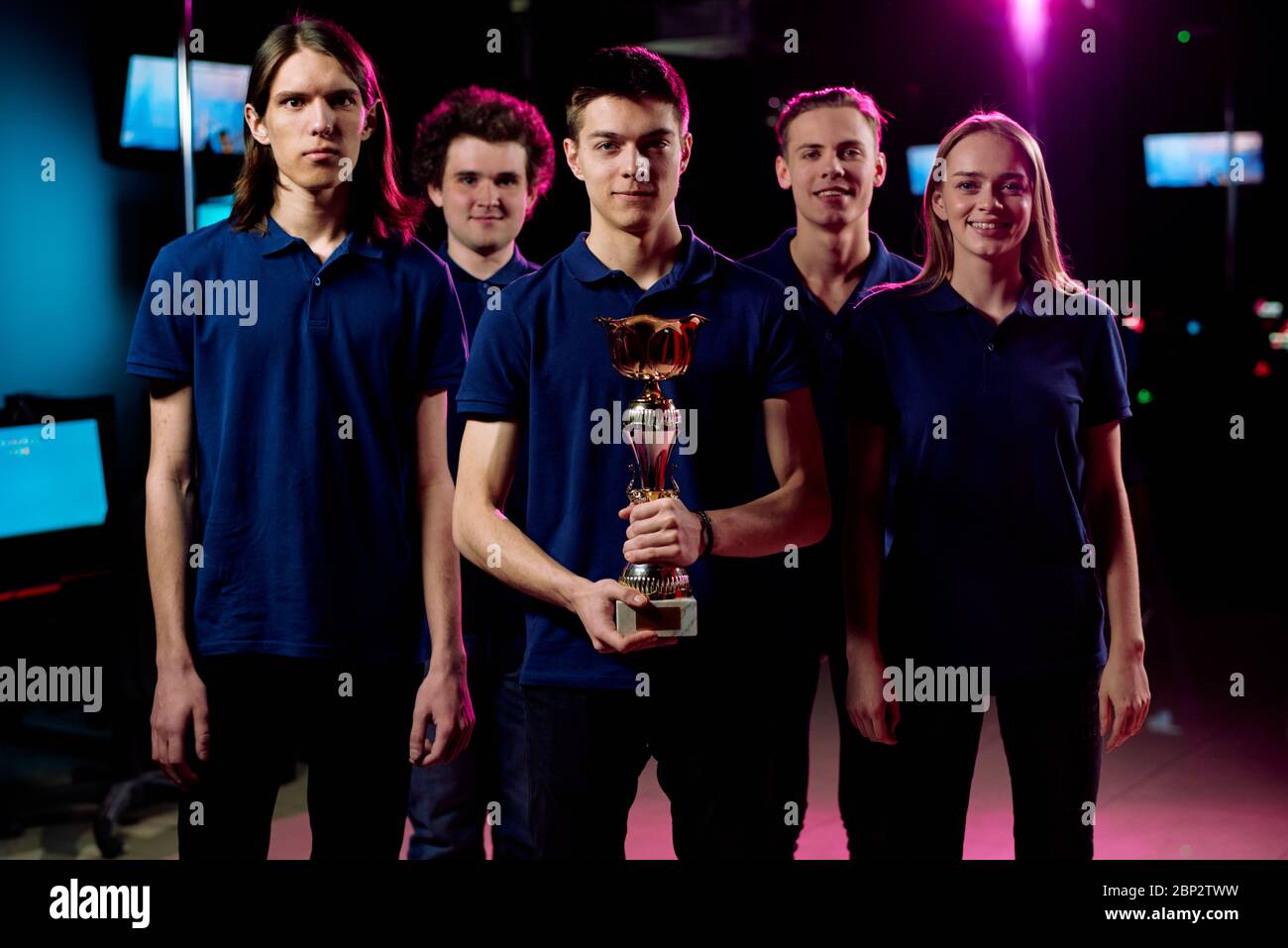 Squadra di cinque giovani campioni di cybersport e di gioco in rete che si trova in fila nel club e-sports contemporaneo Foto Stock