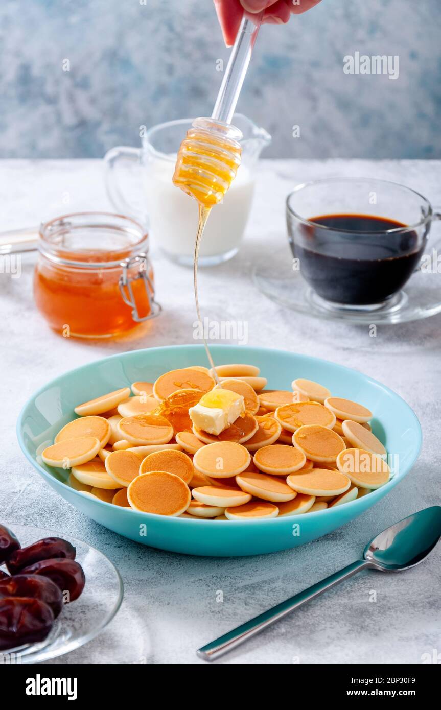 Pancake al cereali con burro e sciroppo di miele o acero gocciolante in ciotola su tavola di pietra grigia. Cucina alla moda. Foto Stock