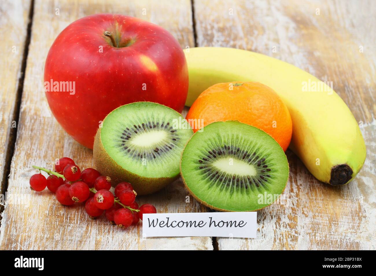 Welcome home card con frutta fresca su superficie di legno: kiwi, mela, banana, corrente rossa, mela Foto Stock