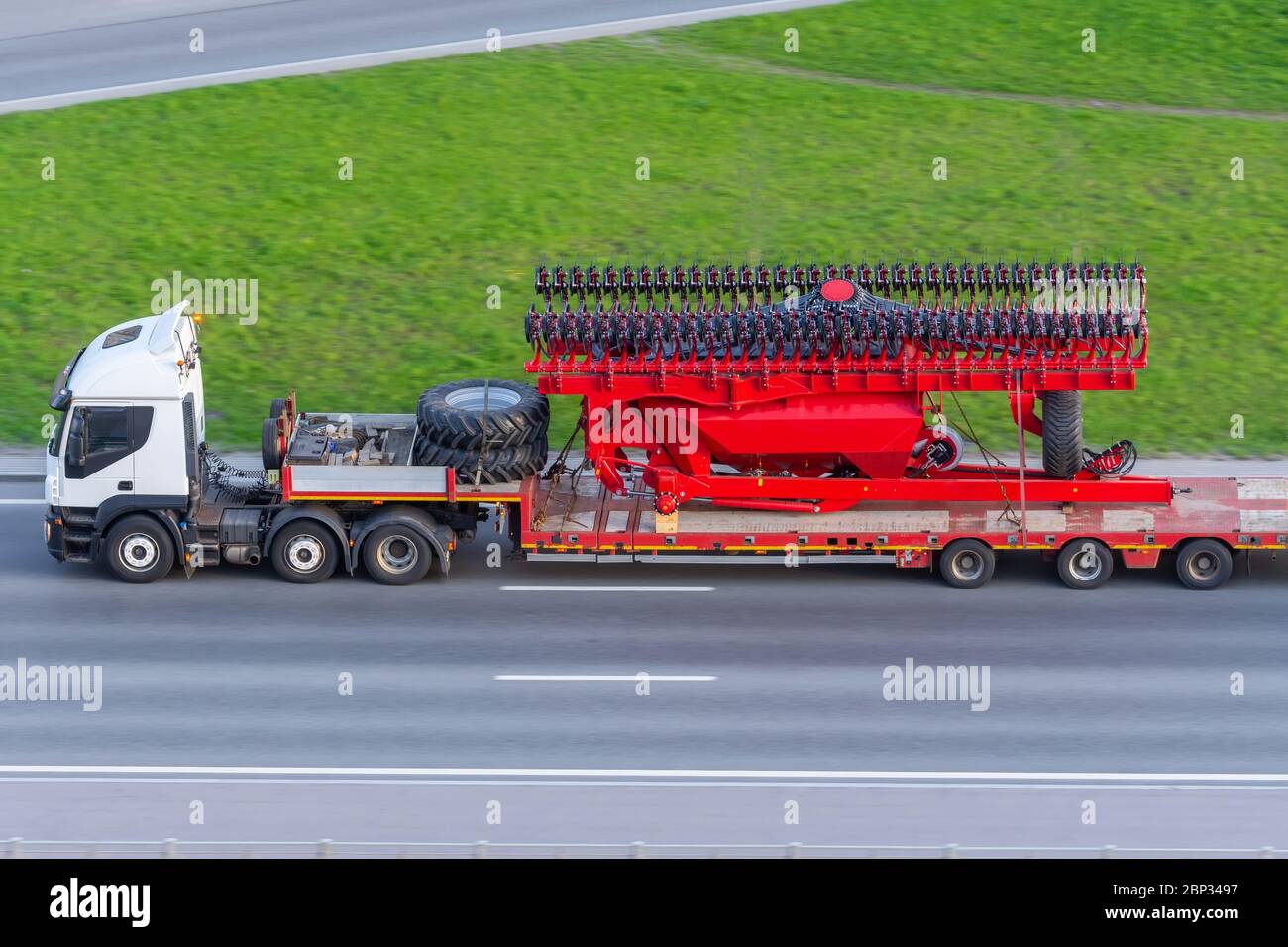 Trasporto di grandi macchine agro-complesse per la coltivazione e la semina di colture su rimorchi lunghi con camion lungo l'autostrada in città Foto Stock