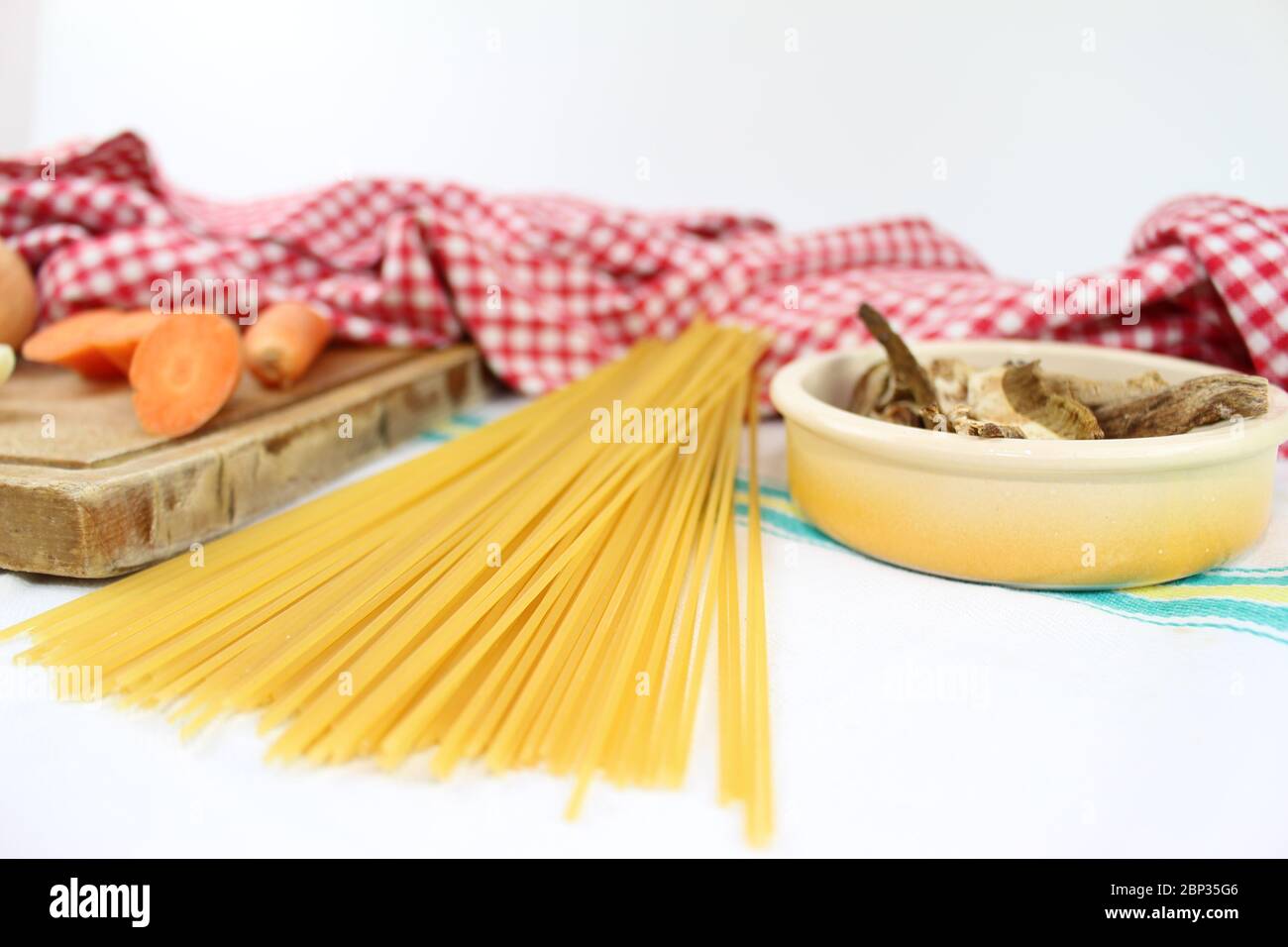 Prodotti alimentari disposti sul tavolo con volant, con quadrati rossi e bianchi. Cucina mediterranea italiana con spaghetti ai funghi porcini secchi. Foto Stock