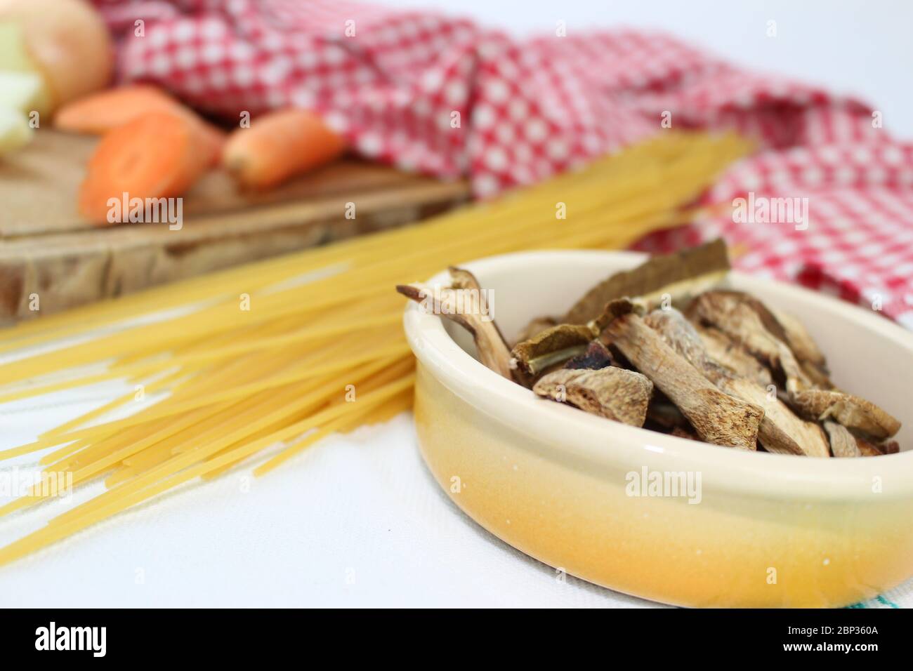 Prodotti alimentari disposti sul tavolo con volant, con quadrati rossi e bianchi. Cucina mediterranea italiana con spaghetti ai funghi porcini secchi. Foto Stock